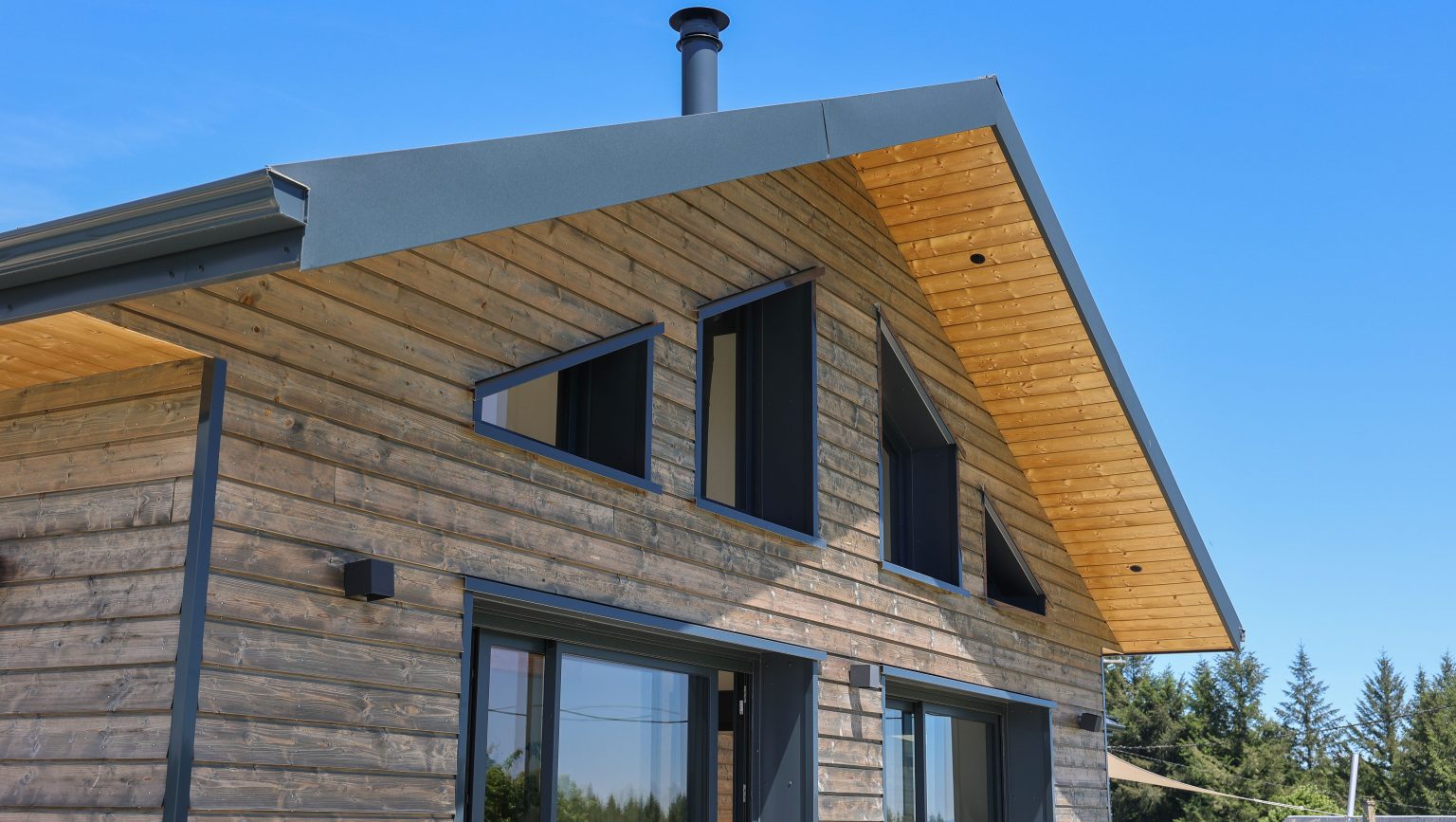 Façade d'une maison ossature bois avec bardage bois gris et menuiseries aluminium